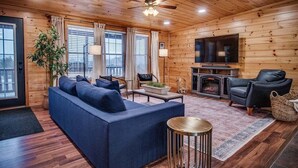 A cozy living room with a blue sofa, a fireplace, a television, and a ceiling fan.
