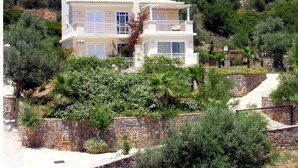 Ein zweistöckiges Haus mit Balkon, umgeben von üppiger Vegetation und einer Steinmauer.