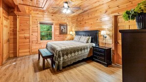 A wooden cabin bedroom with a bed, bench, nightstand, and a window providing a view of the outdoors. - Splash Mansion - Indoor Pool and Theater (Sevierville)
