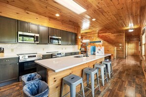 A modern kitchen with stainless steel appliances, wooden cabinetry, and a large island with bar stools. - Splash Mansion - Indoor Pool and Theater (Sevierville)