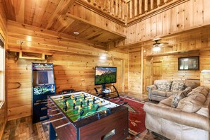 A wooden-floored room with a foosball table, a television, and a sofa. - Splash Mansion - Indoor Pool and Theater (Sevierville)