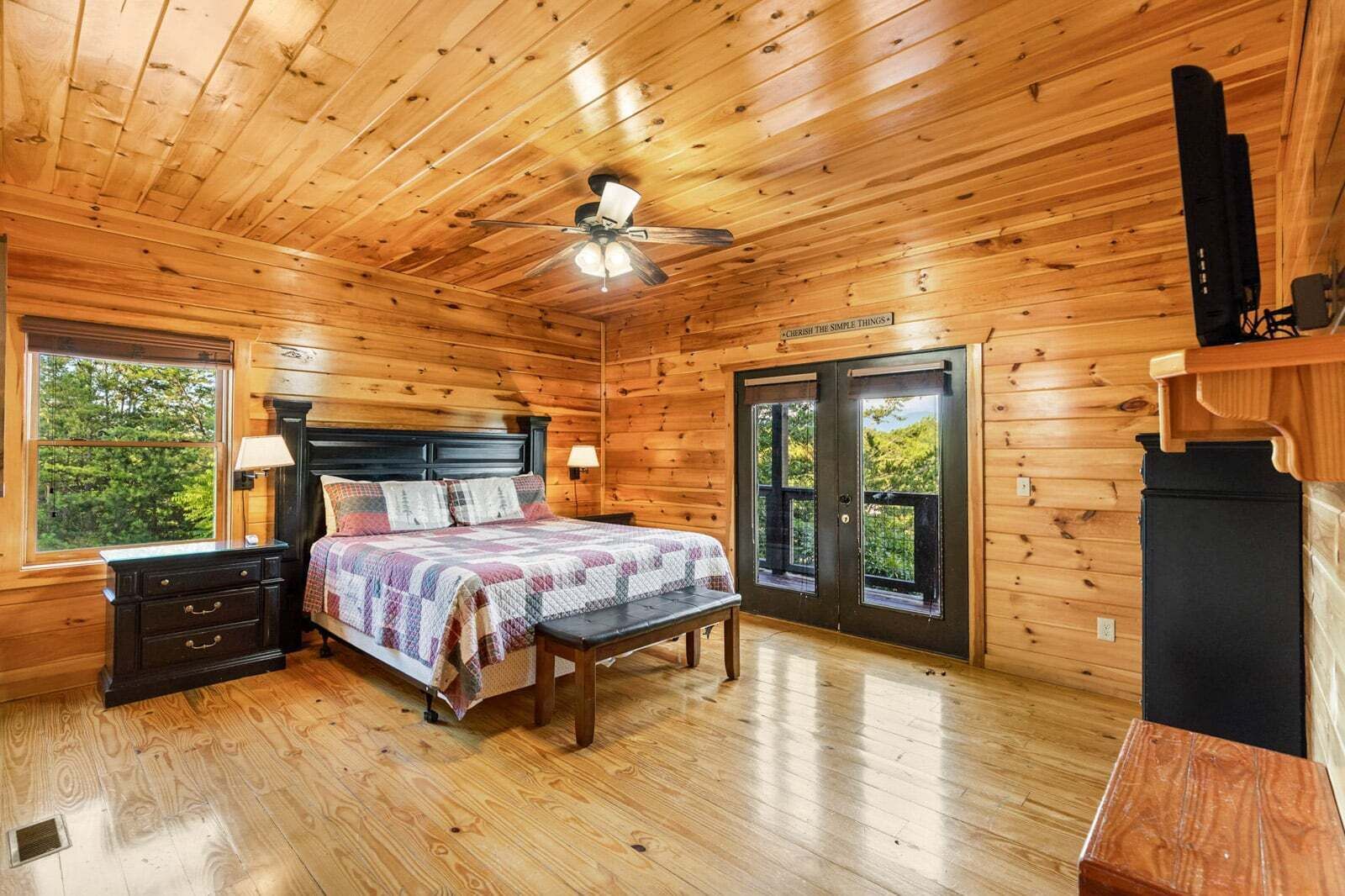 Une chambre dans une cabane en bois, avec un lit, des tables de chevet, un ventilateur de plafond et une fenêtre.