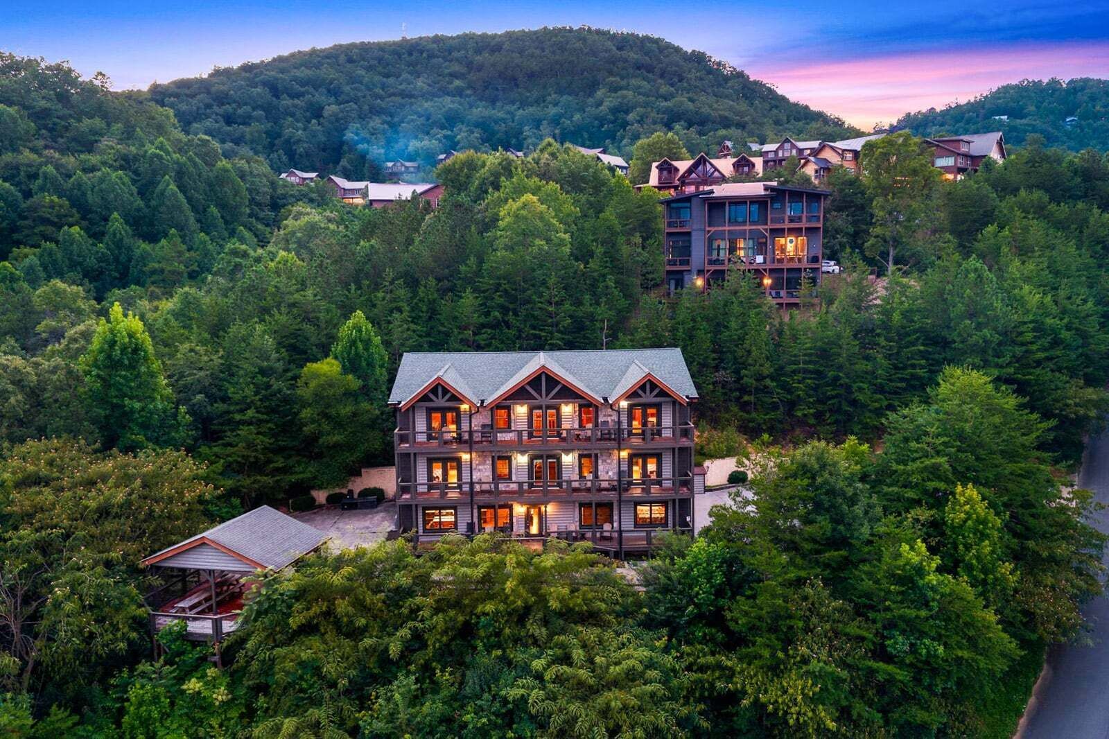 A multi-story lodge with a prominent central building surrounded by dense forest, multiple guest rooms, and a mountain backdrop.