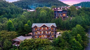 A multi-story lodge with a prominent central building surrounded by dense forest, multiple guest rooms, and a mountain backdrop. - Splash Mansion - Indoor Pool and Theater (Sevierville)