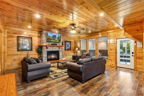 A log cabin interior with a fireplace, two sofas, a television, and a ceiling fan. - Splash Mansion - Indoor Pool and Theater (Sevierville)