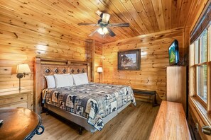 A wooden cabin room with a bed, a desk, a chair, a ceiling fan, and a window. - Splash Mansion - Indoor Pool and Theater (Sevierville)
