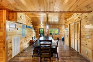 A wooden cabin interior with a dining table, chairs, a window, and a door.