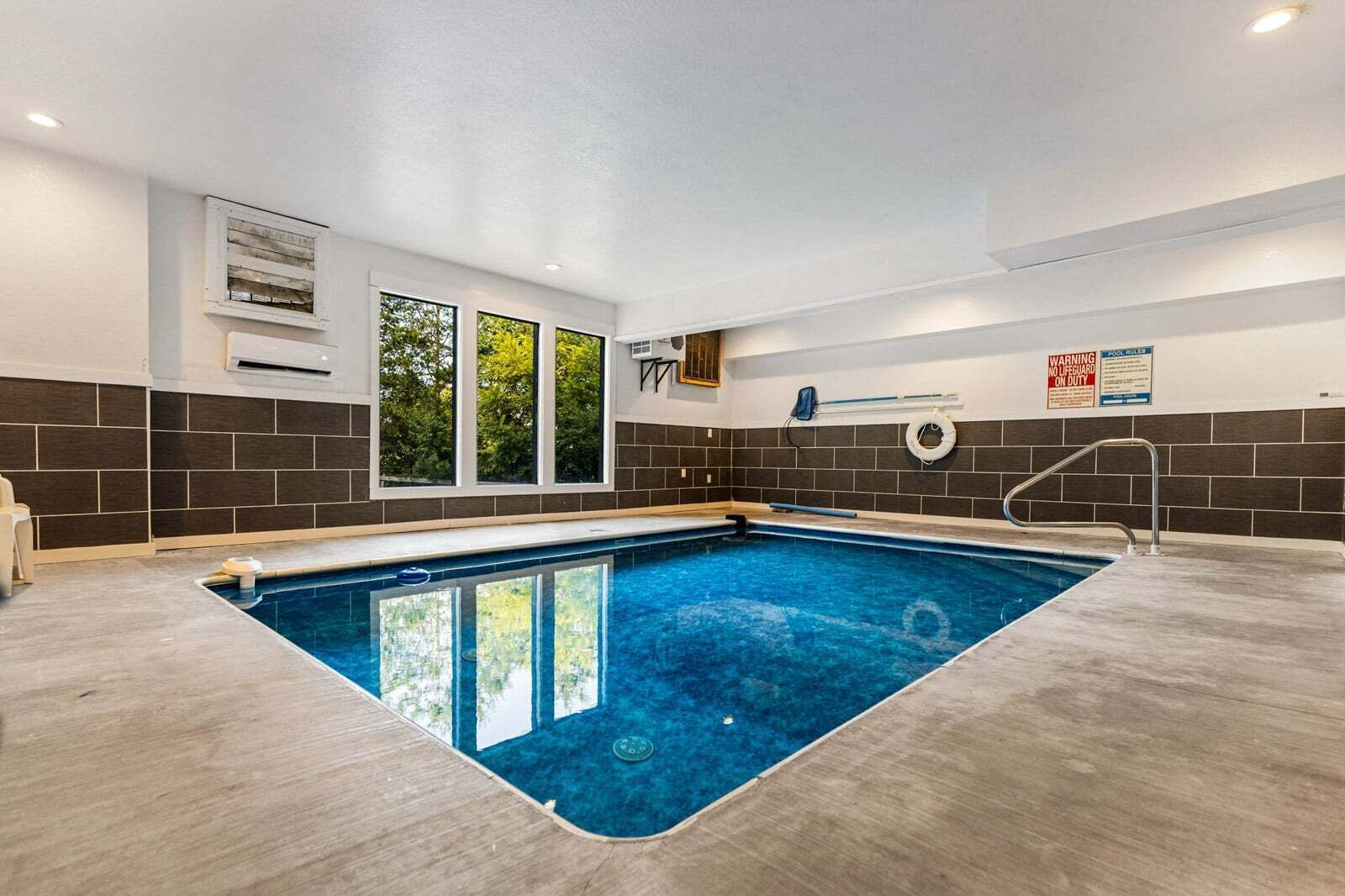 A swimming pool with a tiled deck, a lifeguard stand, and a window with a view of trees.