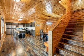 A log cabin interior with a kitchen, dining area, and a staircase. - Splash Mansion - Indoor Pool and Theater (Sevierville)