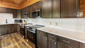 A modern kitchen with dark wood cabinets, stainless steel appliances, and a white countertop. - Splash Mansion - Indoor Pool and Theater (Sevierville)