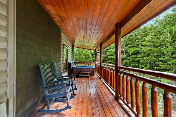 A wooden deck with a hot tub and seating area, overlooking a forested landscape. - Splash Mansion - Indoor Pool and Theater (Sevierville)