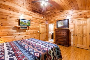 A log cabin bedroom with a bed, a dresser, a television, and a door leading to another room. - Splash Mansion - Indoor Pool and Theater (Sevierville)