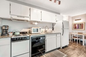 Une cuisine de taille réduite, avec des meubles blancs, une cuisinière, un four à micro-ondes, un évier et un réfrigérateur.