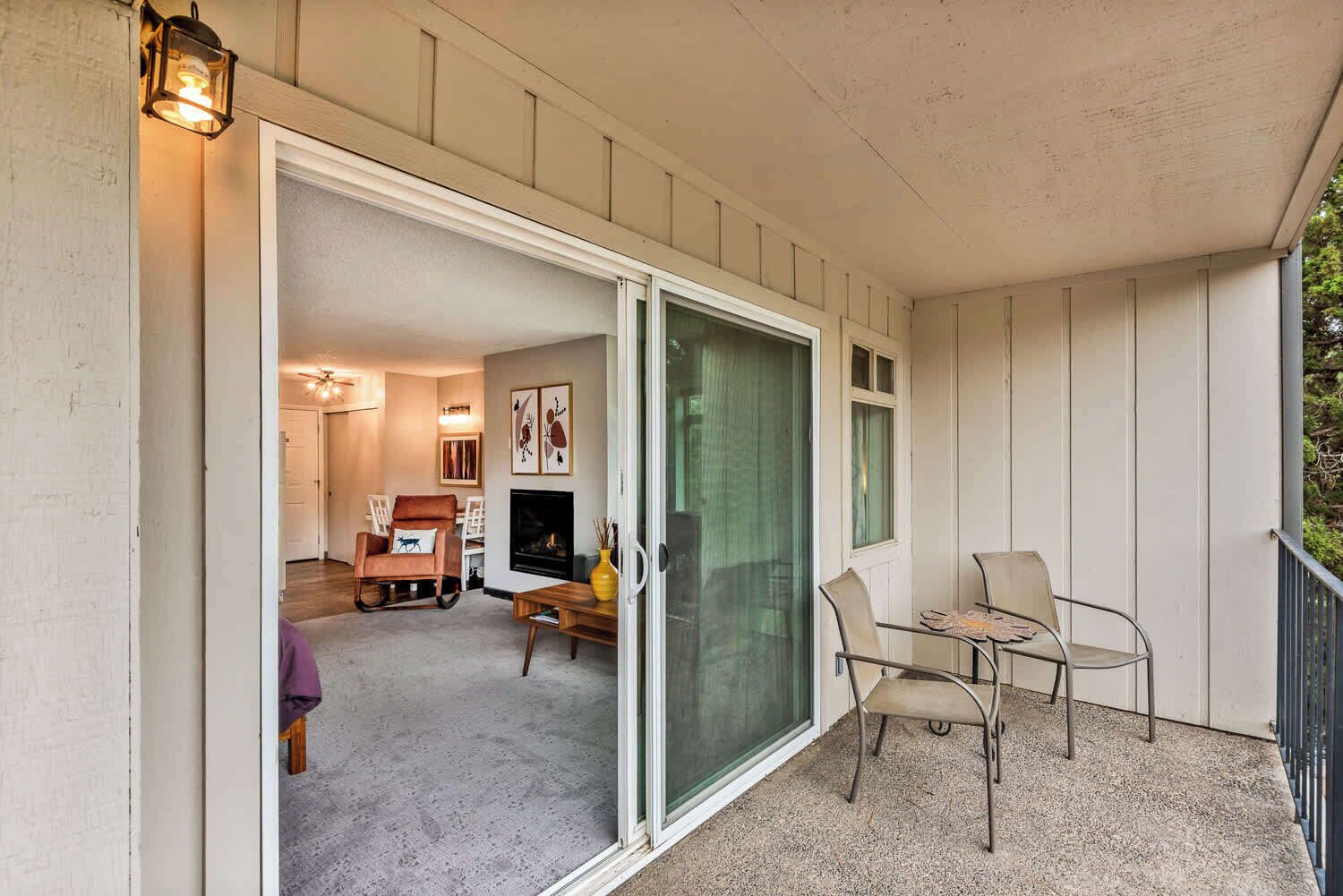 A balcony with a sliding glass door, a chair, a table, and a small fire feature.