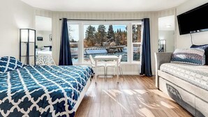 A hotel room with a bed, a sofa, a TV, a desk, and a window with a view of a body of water and trees.