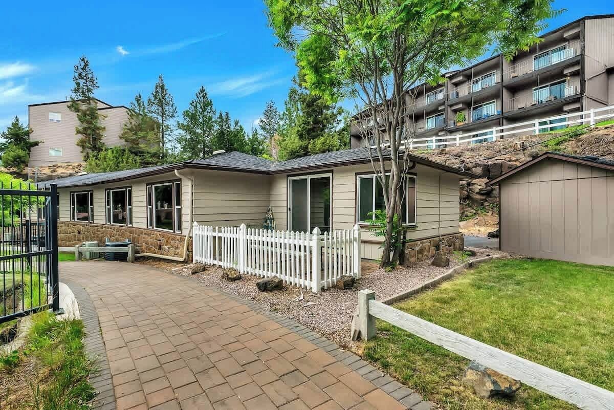 Un immeuble résidentiel avec une allée pavée, une clôture blanche en bois et un petit jardin.