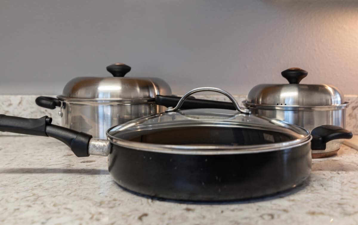 A kitchen with two stainless steel pots and a black pan on a countertop.