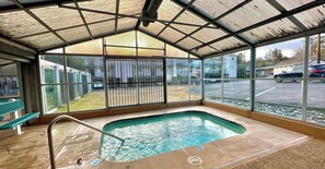 Piscina exterior techada con techo metálico, una banca y vista a un estacionamiento.