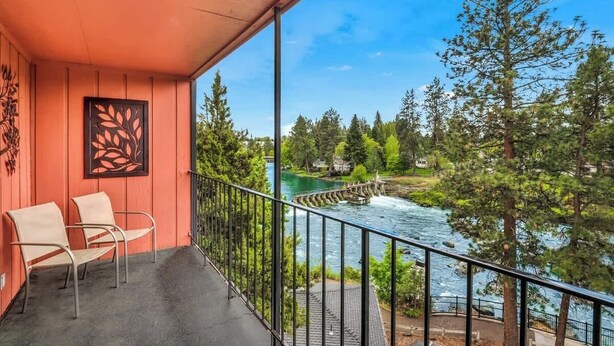A balcony with chairs, a railing, and a view of a river and forest.