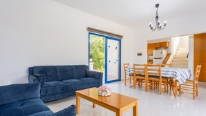 A living room with a blue sofa, a wooden coffee table, and a dining area with a striped tablecloth. - Villa Charoula Tria Large Private Pool, A/C, WiFi (Polis)