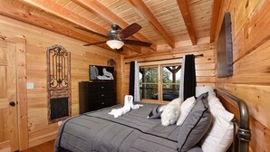 A wooden cabin bedroom with a bed, a dresser, a television, and a window with a view.