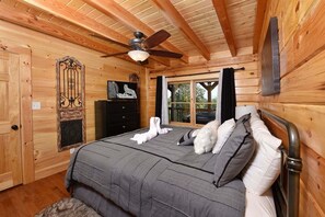 Quarto de cabana de madeira com uma cama, cômoda, televisão e janela com vista.