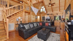 A spacious wooden cabin with a large living area featuring a leather sofa, a dining table, and a kitchen area.