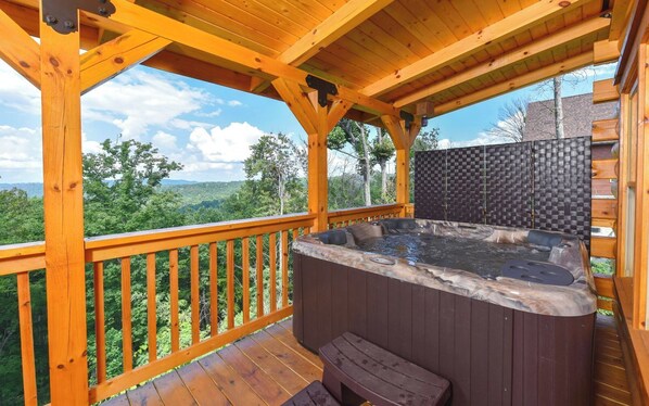 A wooden deck with a hot tub and a bench, overlooking a forested area.