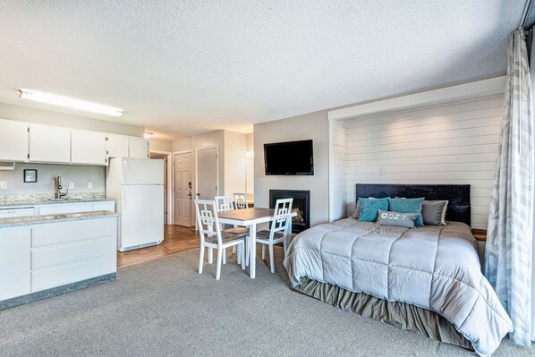 Cozy retreat with a kitchenette and bedroom, featuring a bed, flat-screen TV, and fireplace.