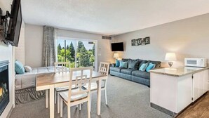 A modern living room with a fireplace, a dining area, a sofa, a TV, and a kitchen area with a microwave.
