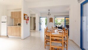 A modern kitchen with wooden cabinets, a built-in microwave, and a dining area with a round wooden table and chairs. - Villa Charoula Pente (Polis)