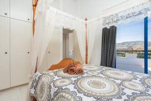 A bedroom with a bed, a canopy, a view of the outdoors, and a window with curtains. - Villa Charoula Pente (Polis)