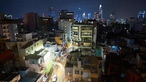 Une vue nocturne d’une ville, avec un mélange de bâtiments modernes et plus anciens, une rue animée où circulent des voitures, et un bâtiment remarquable qui se distingue par son architecture originale.