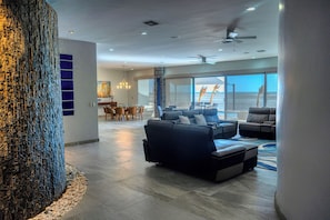Een ruime woonkamer met een grote boomsculptuur, moderne meubels en uitzicht op de oceaan.