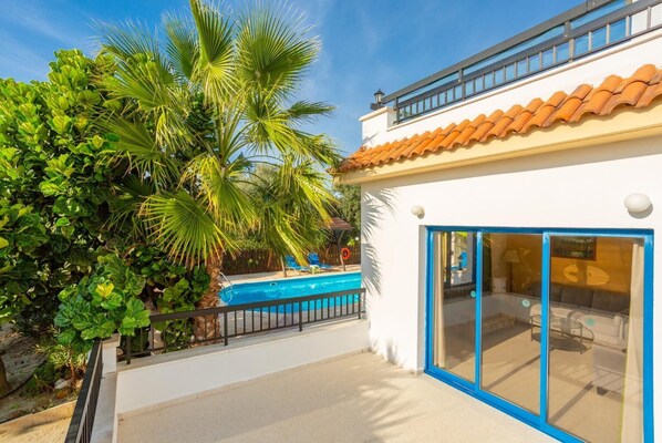 Ett modernt hus med en swimmingpool, omgivet av frodig grönska och palmer.