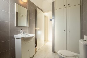 Ein modernes Badezimmer mit Waschbecken, Spiegel und Toilette in Weiß, sowie ein Kleiderschrank mit zwei Türen.