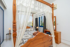 Ein Bett mit Baldachin, ein Nachttisch, ein Spiegel und Blick ins Freie.