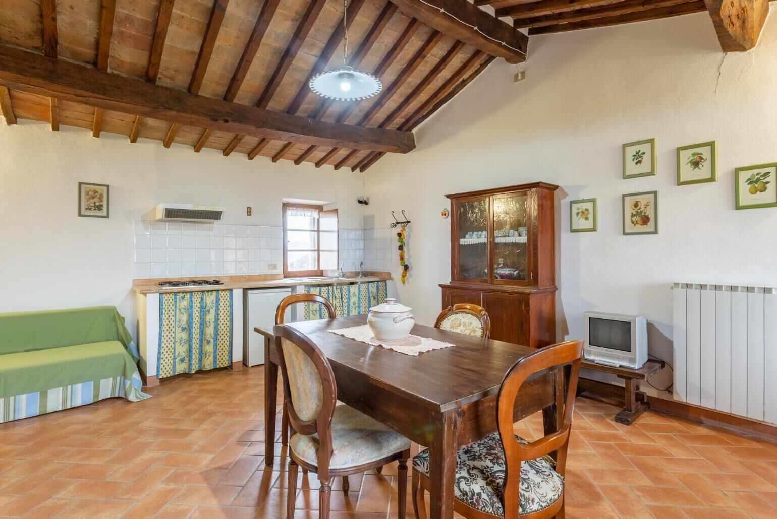 A rustic kitchen with wooden beams, a dining table with chairs, a cabinet, and a television.