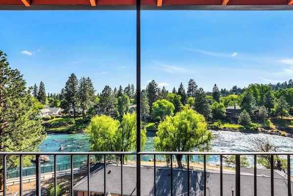 A balcony with a view of a river, trees, and houses in the background.