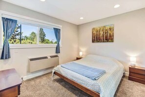 Une chambre à coucher avec un lit, une fenêtre avec des rideaux, un radiateur, une table de chevet et une commode, ainsi qu’une œuvre d’art accrochée au mur.