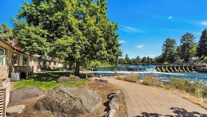 A riverside walkway with a wooden deck, large rocks, and a tree. - Cozy one-bedroom condo overlooking the Deschutes (Bend)