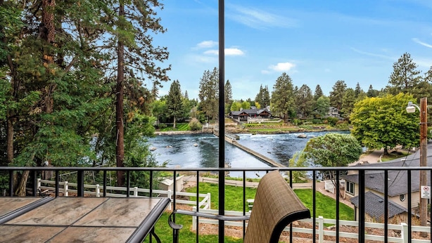 A river view from a balcony with a table and chair, surrounded by trees and houses. - Cozy one-bedroom condo overlooking the Deschutes (Bend)