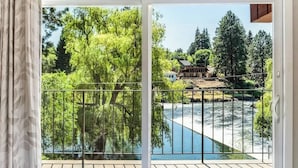 A balcony with a view of a river, trees, and a house in the background. - Cozy one-bedroom condo overlooking the Deschutes (Bend)