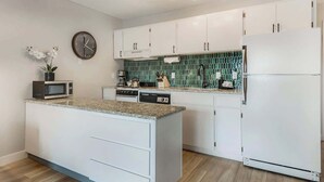 A modern kitchen with white cabinetry, a granite countertop, a built-in microwave, a coffee maker, and a refrigerator. - Cozy one-bedroom condo overlooking the Deschutes (Bend)