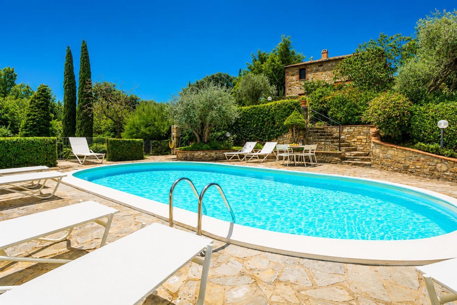 A swimming pool with lounge chairs and a stone wall.
