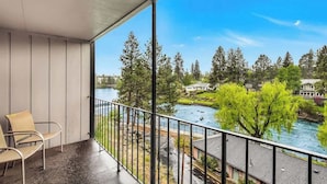 Un balcón con sillas, vista a un río, árboles y casas.