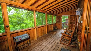 A wooden cabin with a porch, large windows, and a metal table.