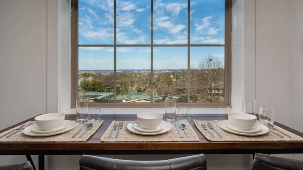 Mesa de comedor para cuatro personas con vista a un paisaje urbano a través de un gran ventanal.
