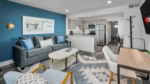 Un apartamento moderno con un sofá gris, una mesa de centro blanca y una zona de comedor con una mesa y sillas de madera.