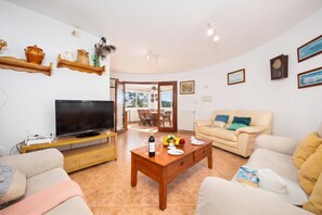 A living room with a TV, wooden coffee table, sofa, and a dining area with chairs.